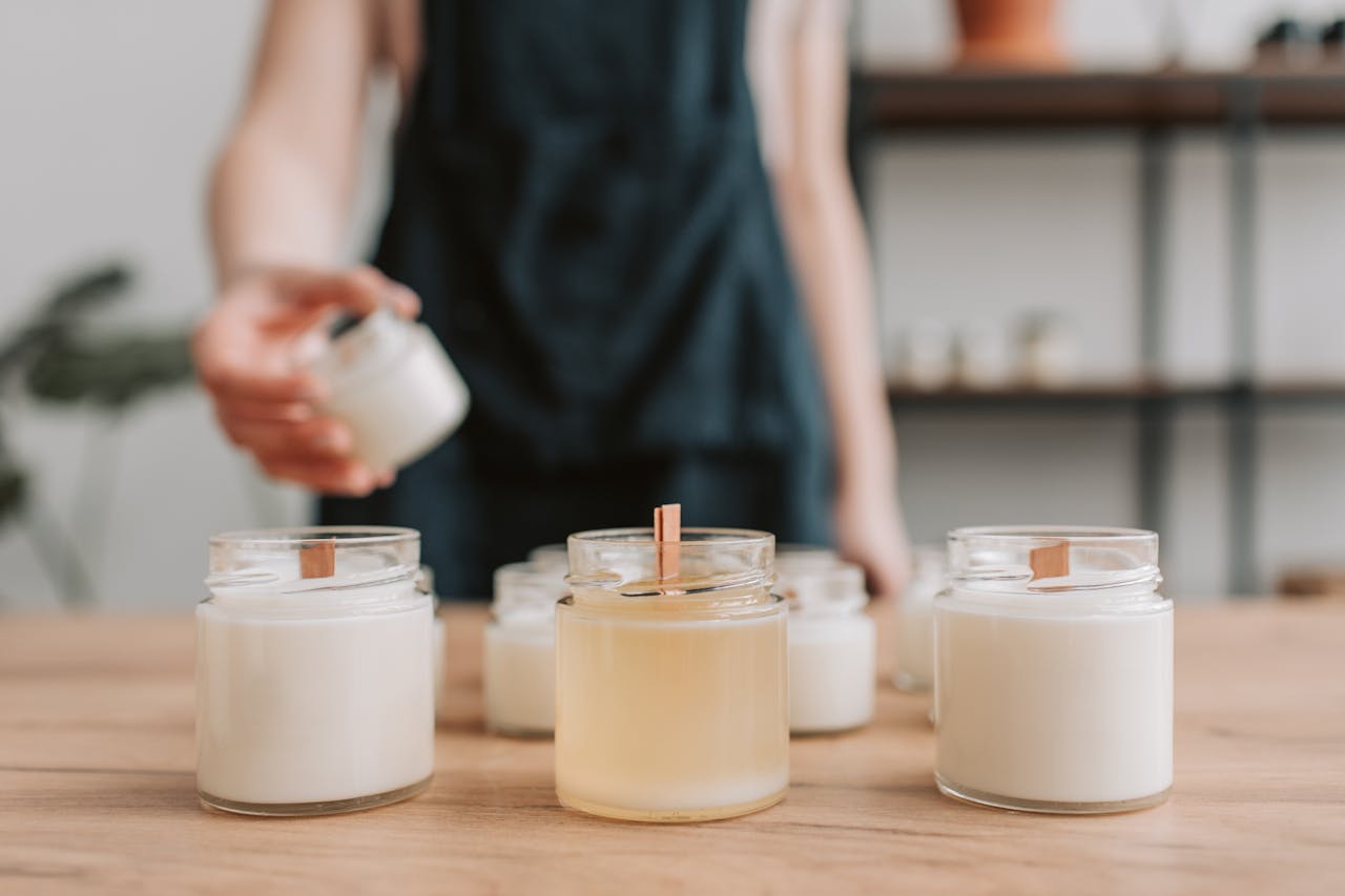 A woman making artisanal soy candles on a wooden table, showcasing a small business workshop setting.
